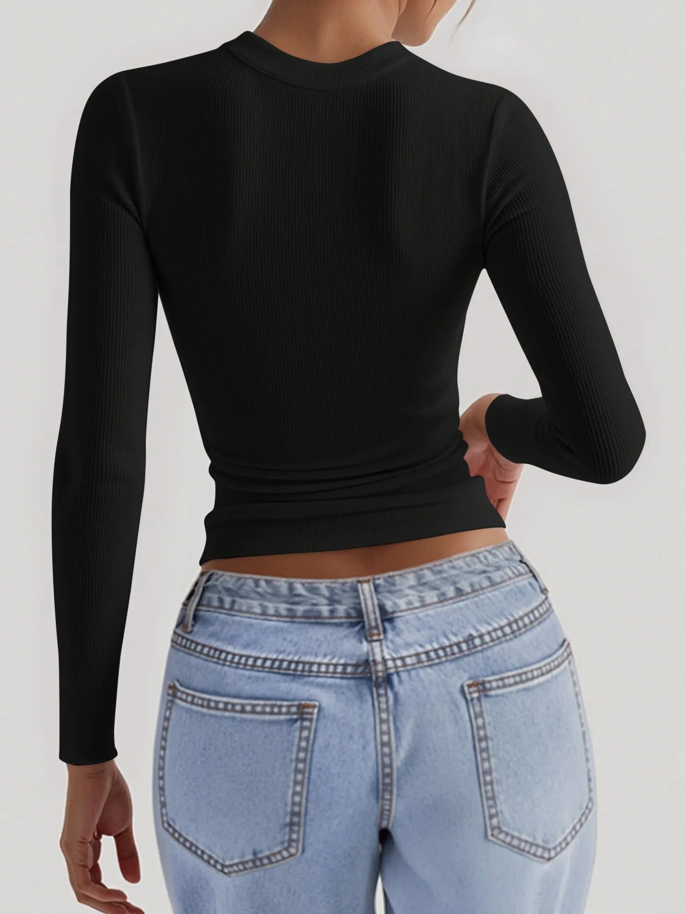 Person wearing a black long-sleeve top and light blue jeans on a white background