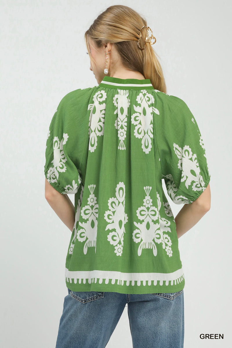 Green blouse with white patterns worn by a person on a white background