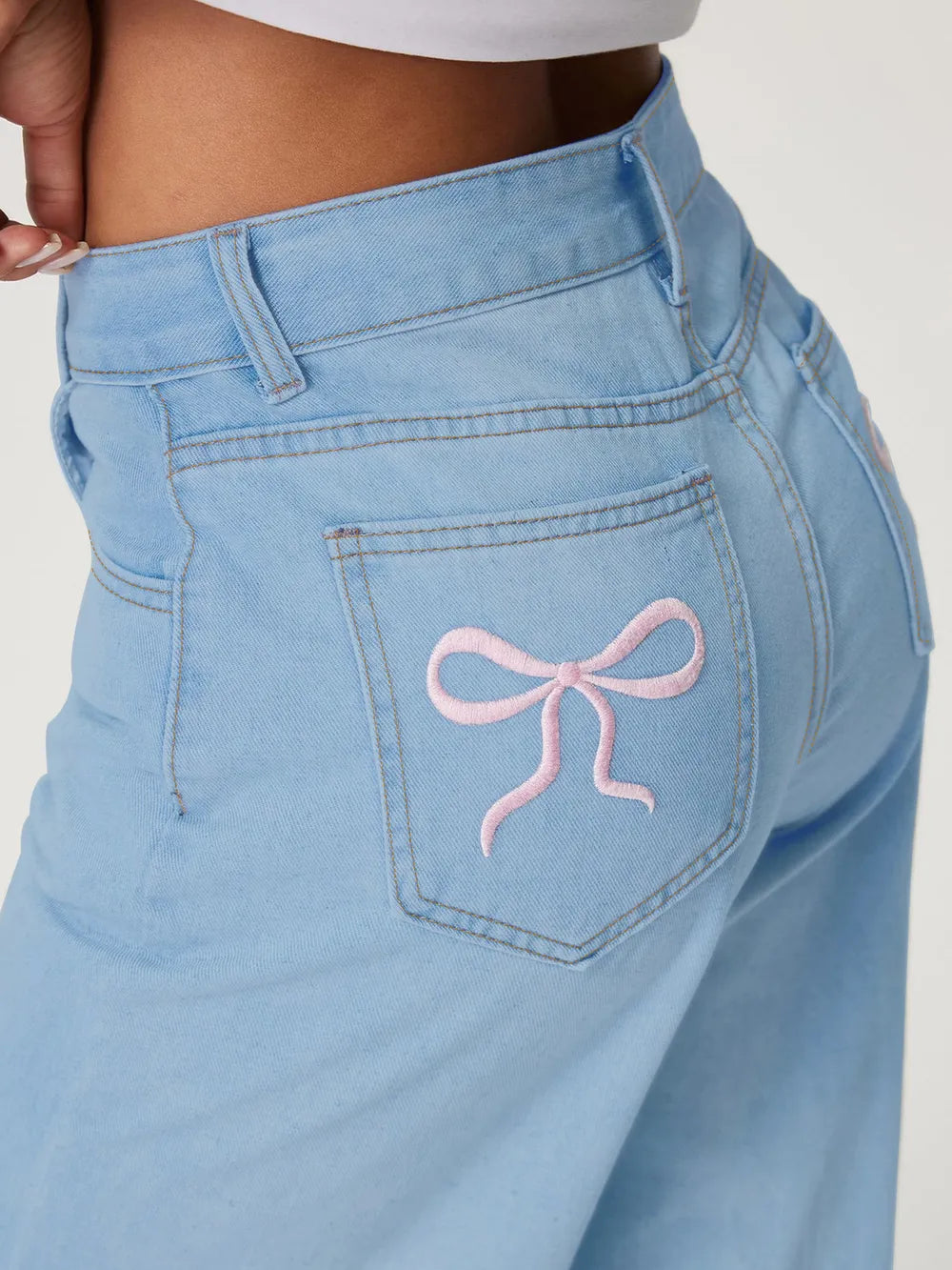 Light blue jeans with a pink bow design on the pocket against a white background