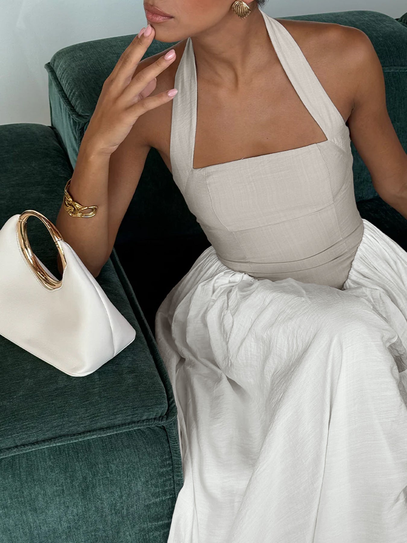 Woman in a white dress sitting on a green couch with a white handbag next to her.