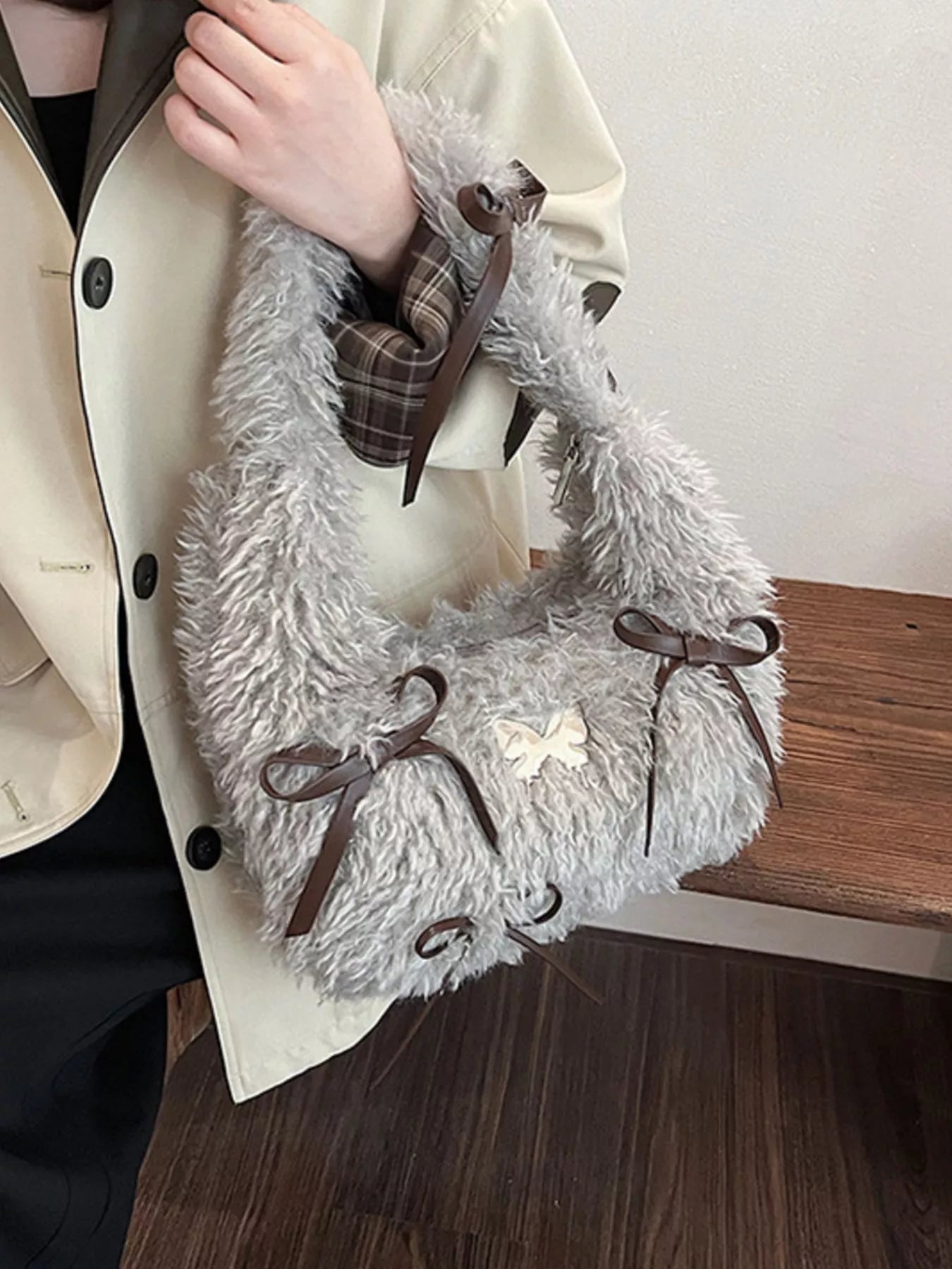 Gray fluffy bag with brown ribbons held by a person wearing a beige coat.