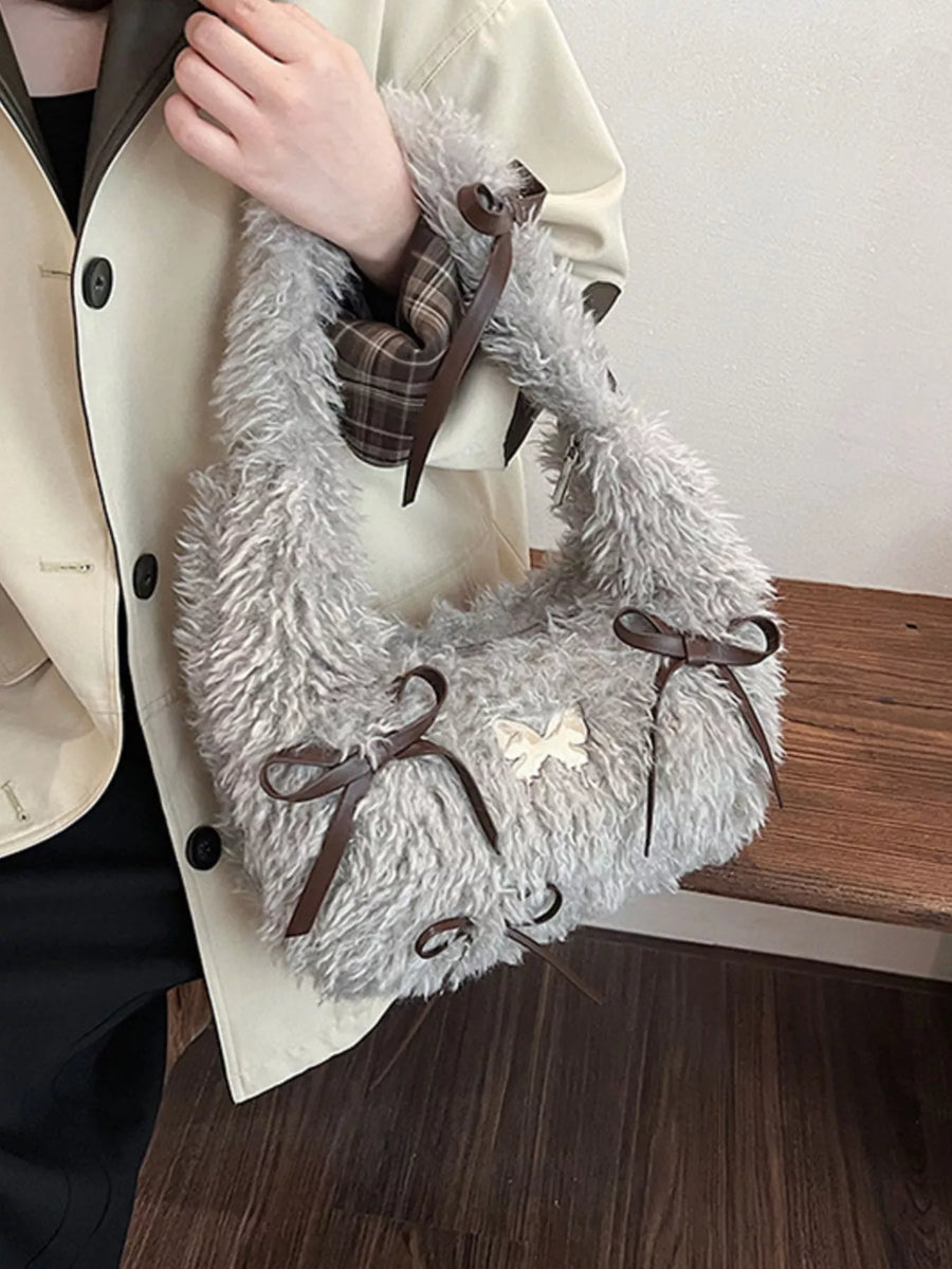 Gray fluffy bag with brown ribbons held by a person wearing a beige coat.