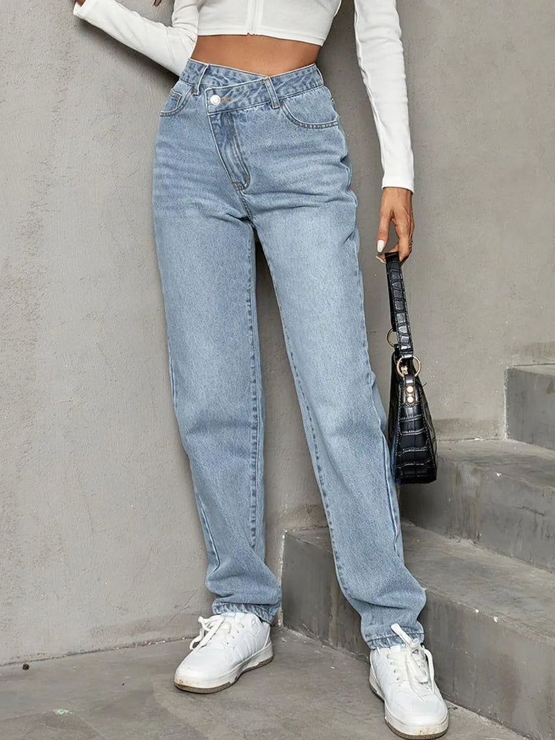 Person wearing light blue jeans and white sneakers against a gray concrete wall.