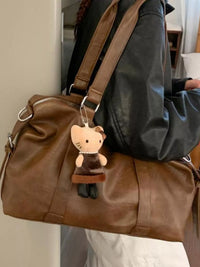 Brown leather bag with a Hello Kitty keychain held by a person wearing a black jacket.