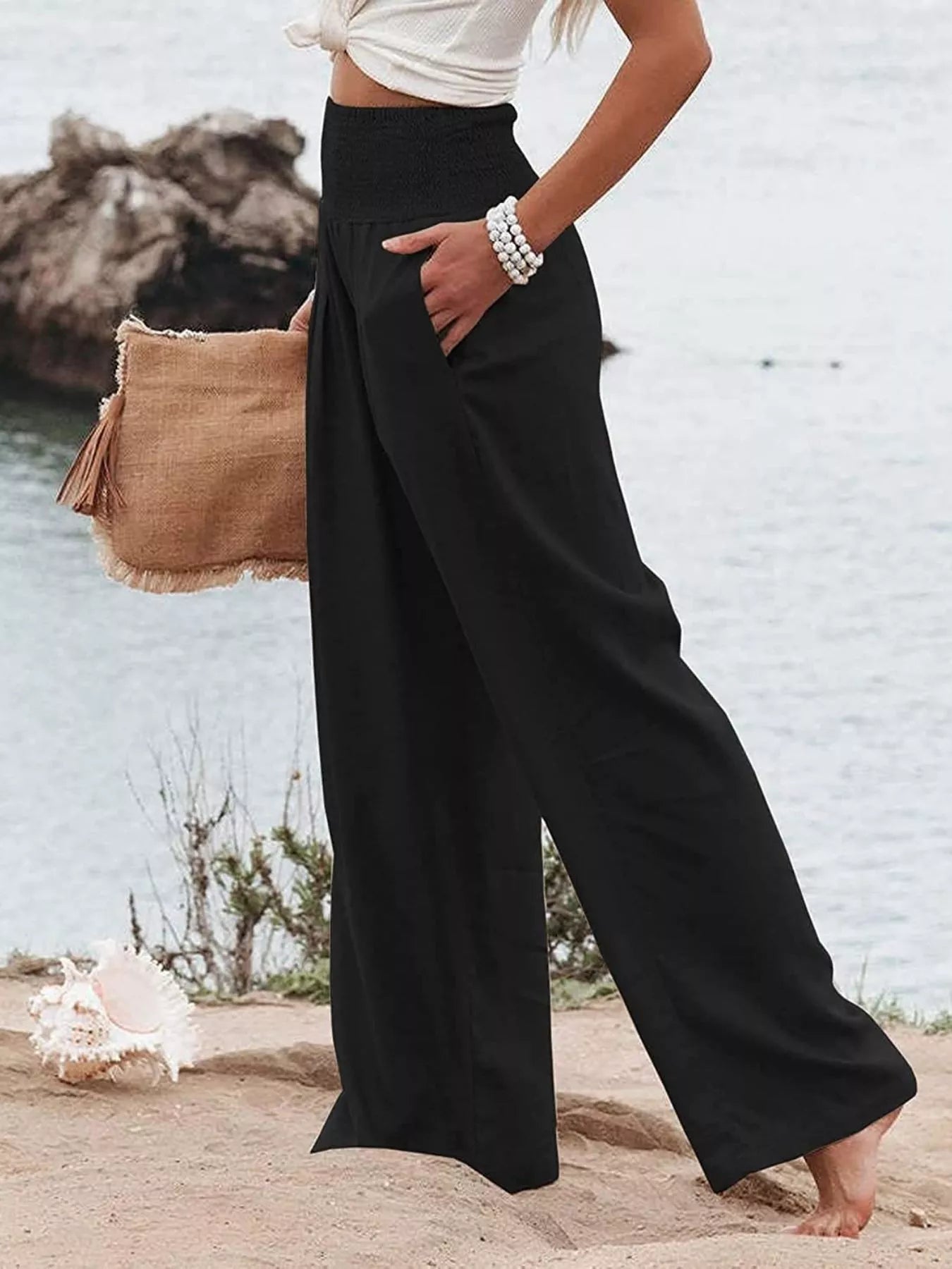 Person wearing black wide-leg pants and a white top by a body of water.