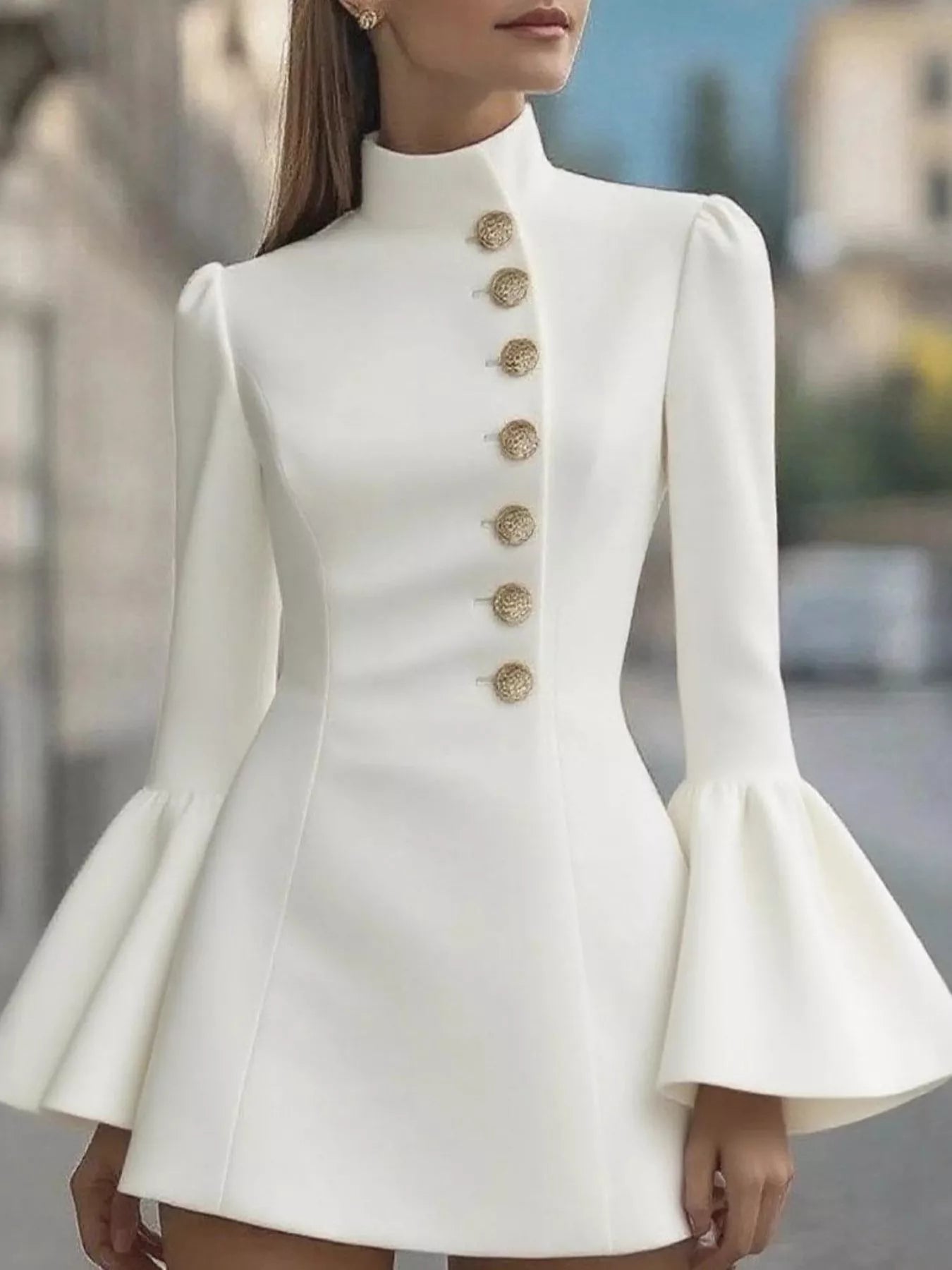White dress with gold buttons and flared sleeves worn by a model outdoors.