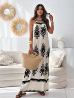 Woman in a white dress with black patterns holding a beige bag in a living room.