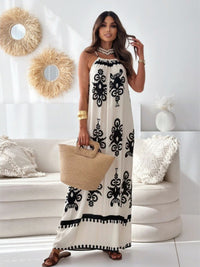 Woman in a white dress with black patterns holding a beige bag in a living room.
