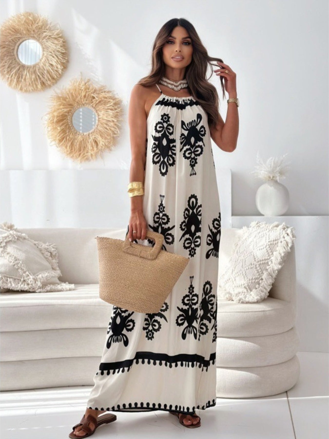 Woman in a white dress with black patterns holding a beige bag in a living room.