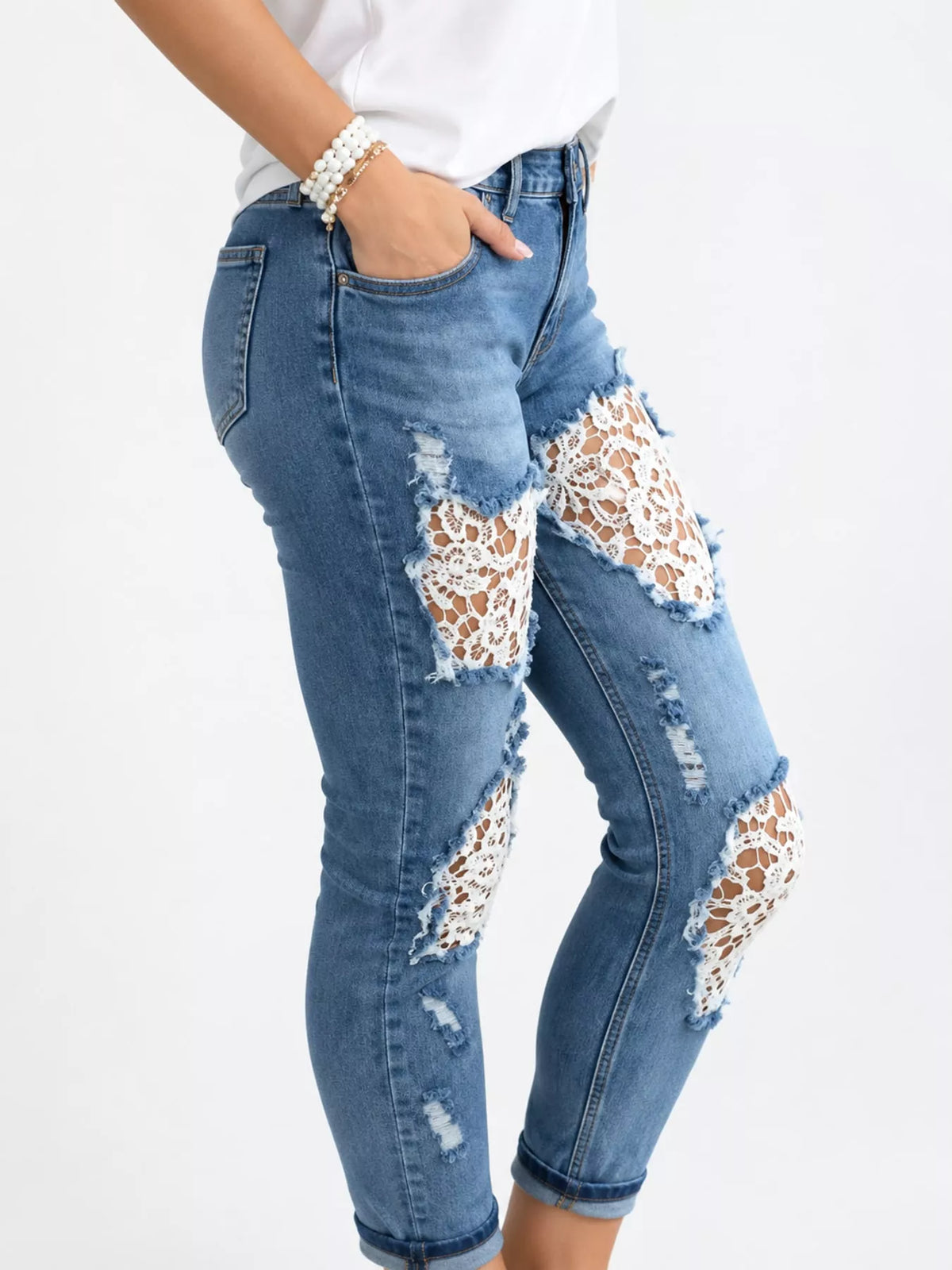 A person wearing blue distressed skinny jeans with large white lace patch details on the thighs and knees, paired with a white top against a plain white background.