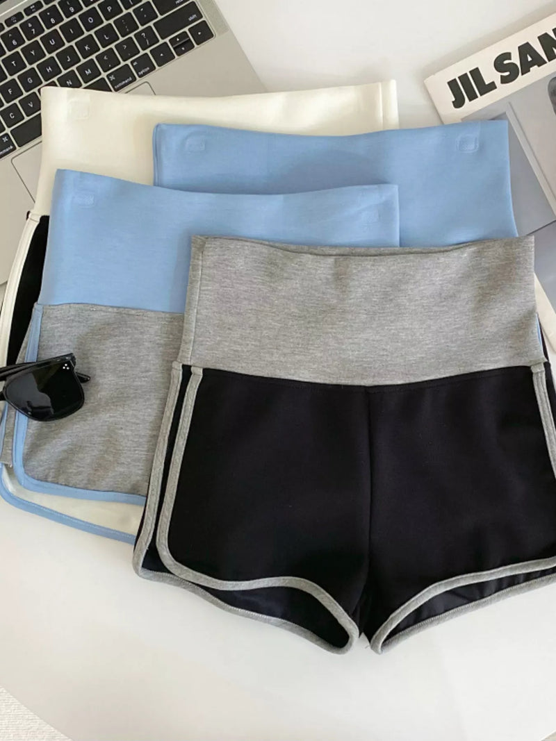 Set of black, gray, and blue shorts on a white surface with a laptop and keyboard in the background.