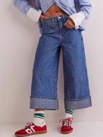 Person wearing blue jeans, a light blue shirt, and red sneakers on a plain background