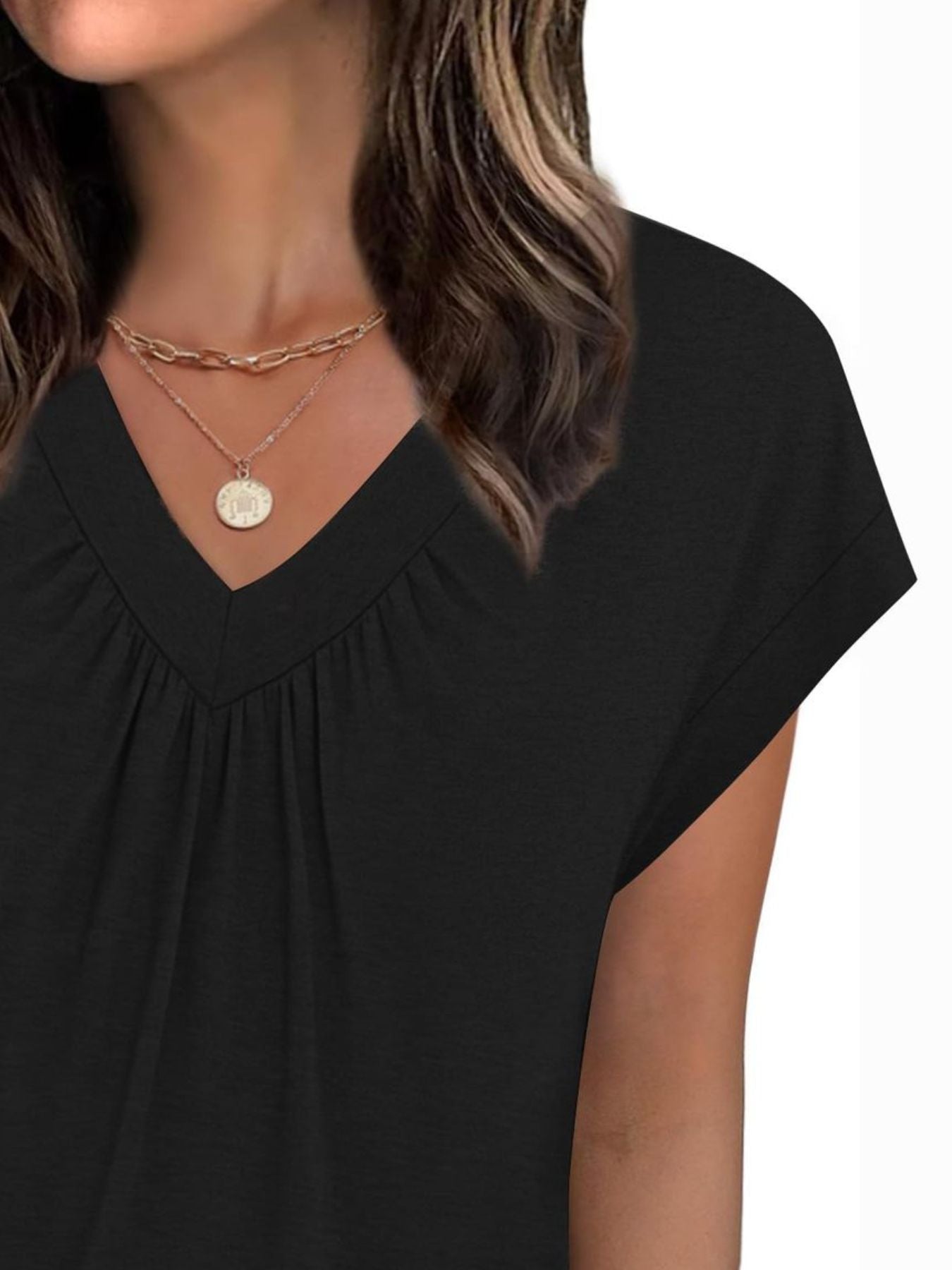 Black top worn by a person with layered necklaces on a white background