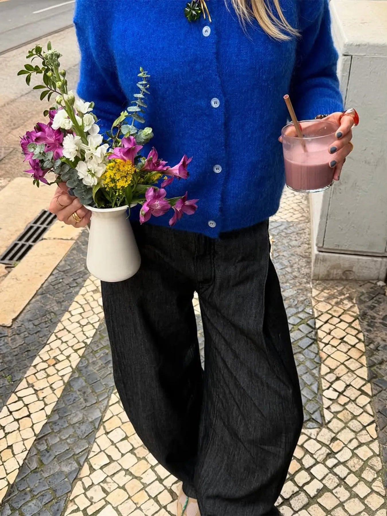 Person holding a cup of coffee and a small bouquet of flowers on a street.