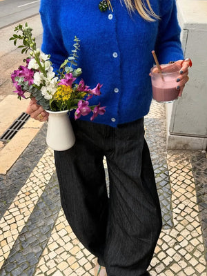 Person holding a cup of coffee and a small bouquet of flowers on a street.