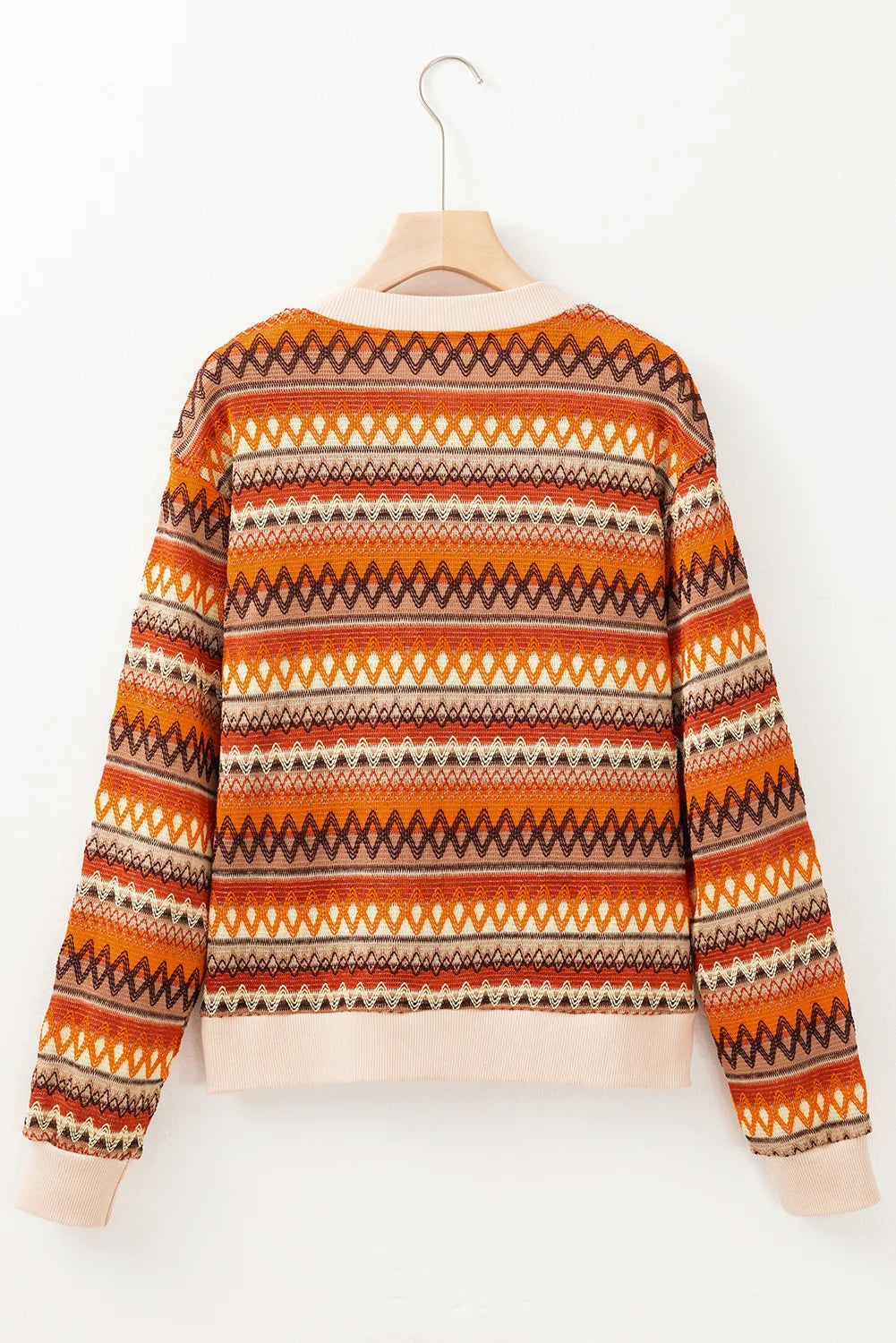 Orange and brown patterned sweater on a hanger against a white background