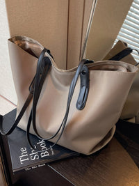 Beige handbag with black straps on a wooden surface