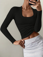 Person wearing a black long-sleeve top and light gray pants against a neutral background
