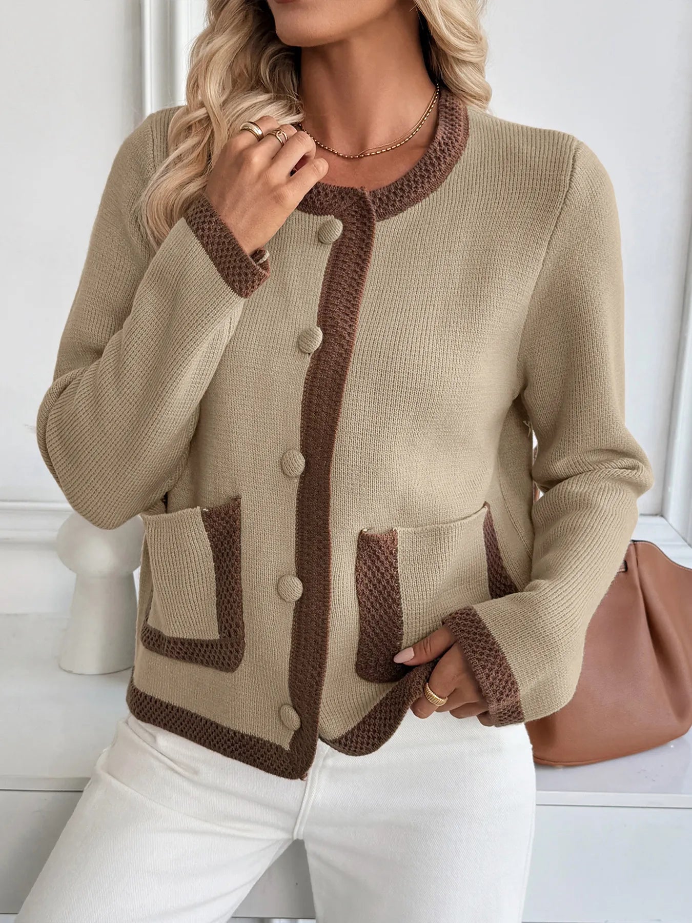 Woman wearing a beige cardigan with brown accents and white pants.