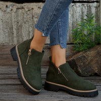 Green suede ankle boots with zippers worn by a person on a wooden floor.