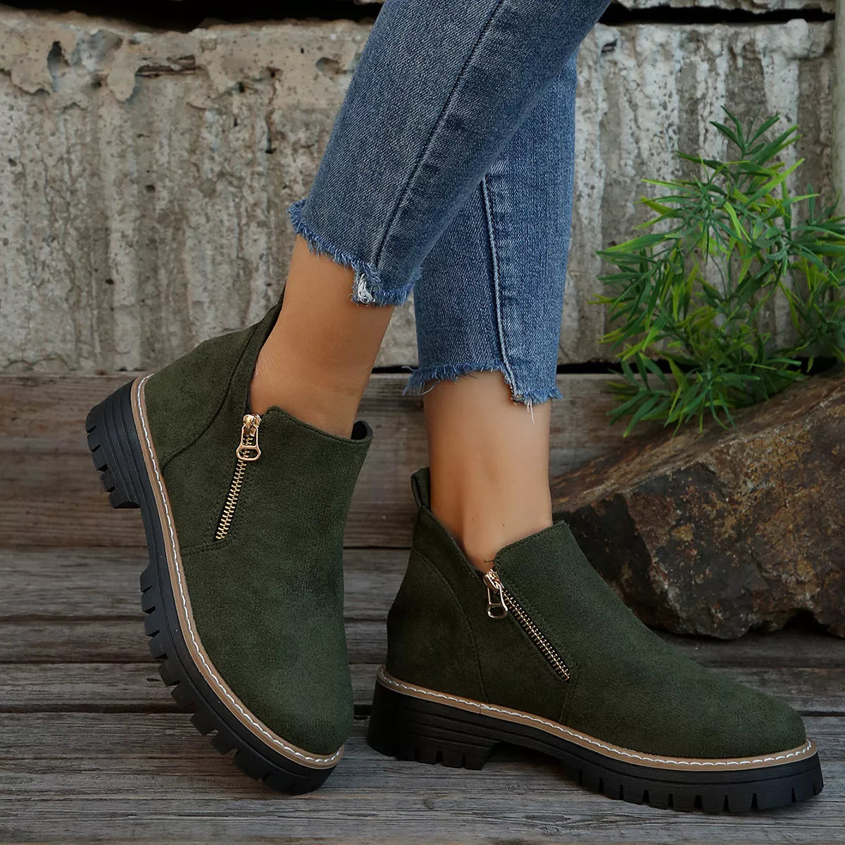 Green suede ankle boots with zippers worn by a person on a wooden floor.