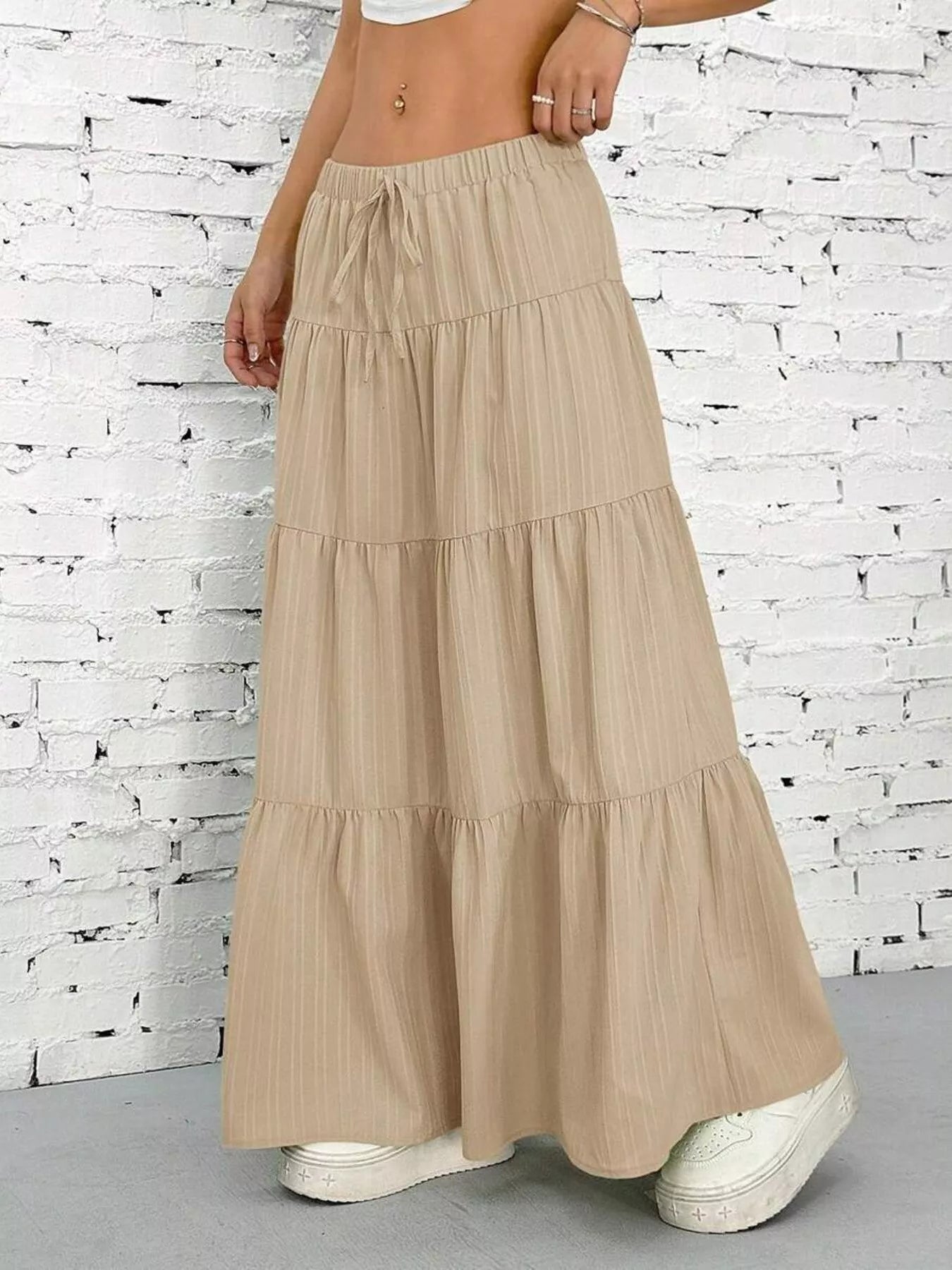Beige tiered skirt worn by a person against a white brick wall.