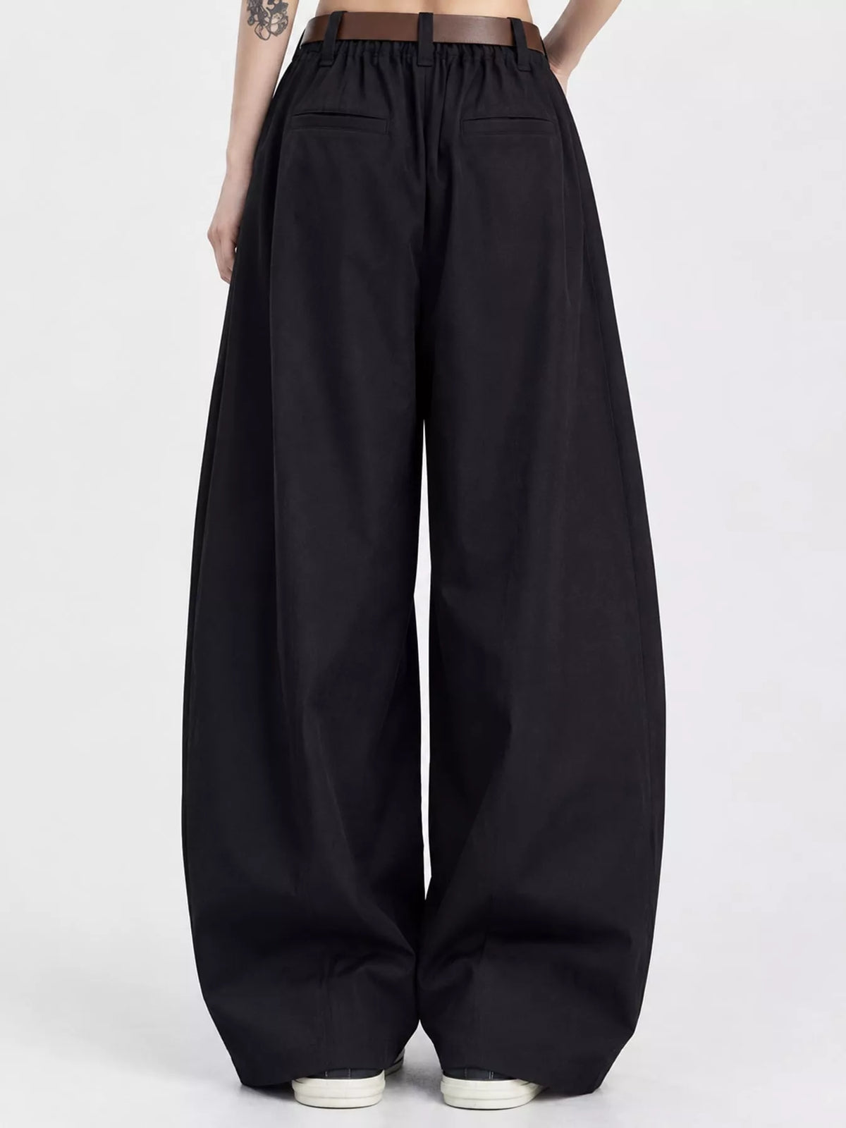Black wide-leg pants with an elastic drawstring waist and front patch pockets, shown on a model from the back against a light gray studio background.
