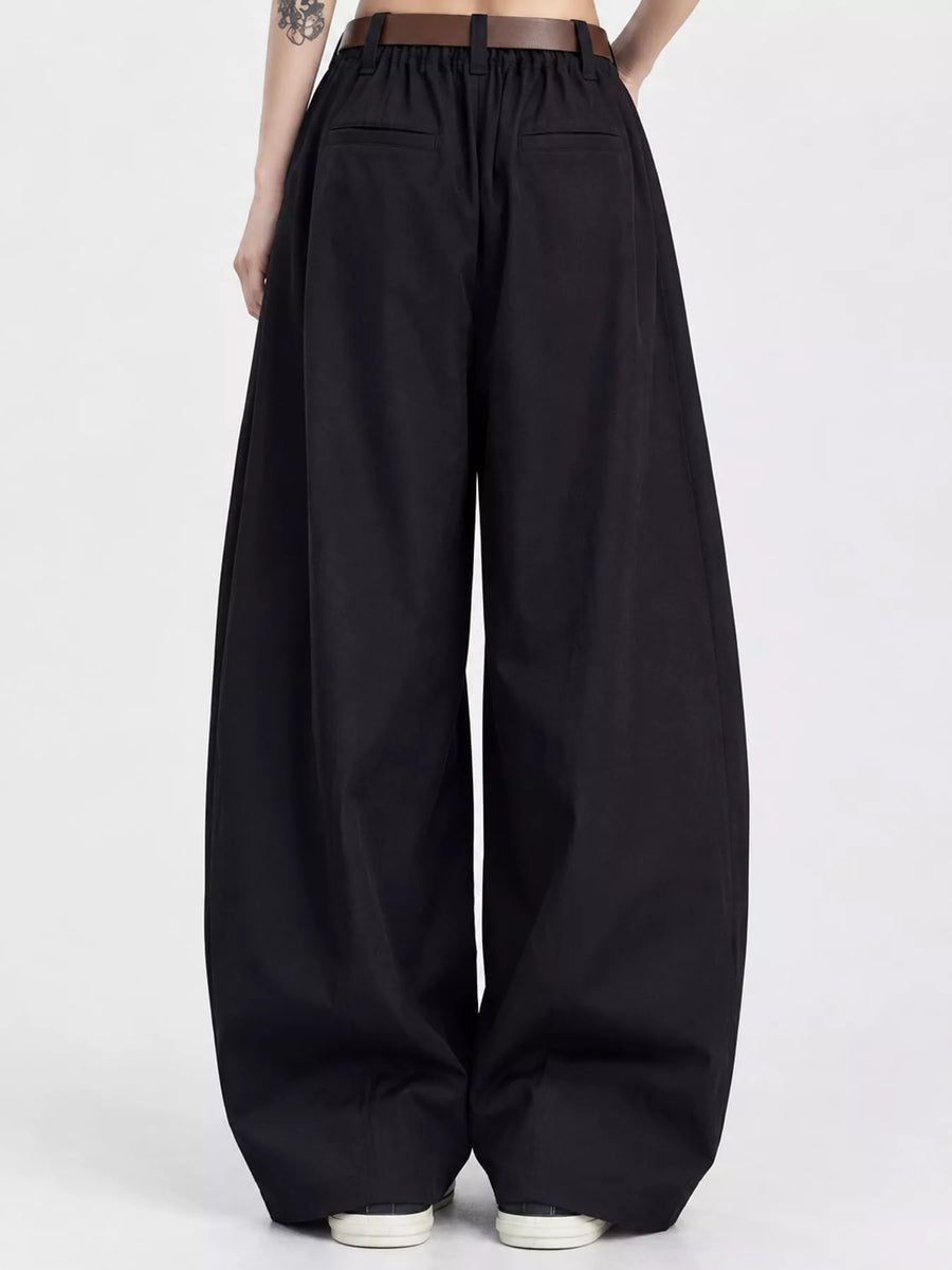 Black wide-leg pants with an elastic drawstring waist and front patch pockets, shown on a model from the back against a light gray studio background.