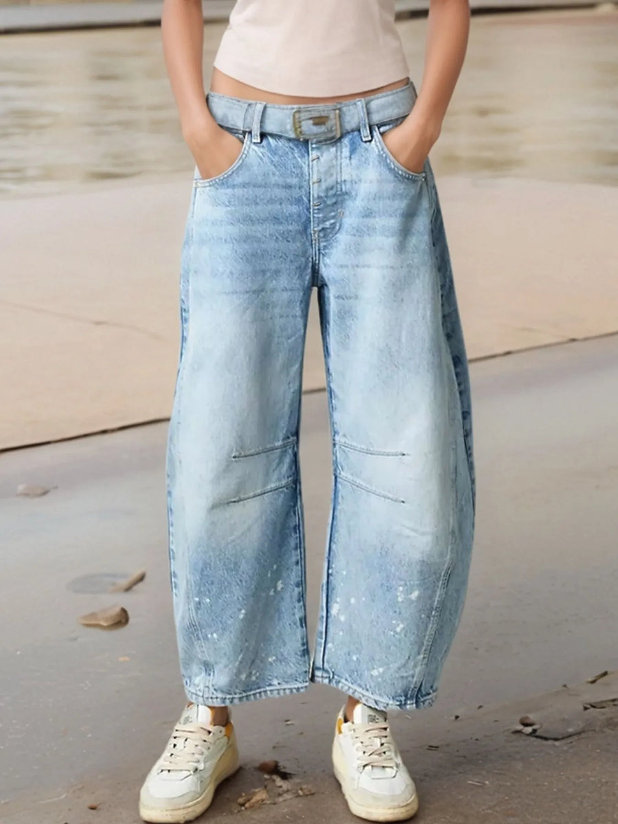 Person wearing light blue wide-leg jeans and white sneakers on a neutral background