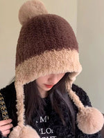 Person wearing a brown and beige fur-trimmed hat with pom-poms on a plain background