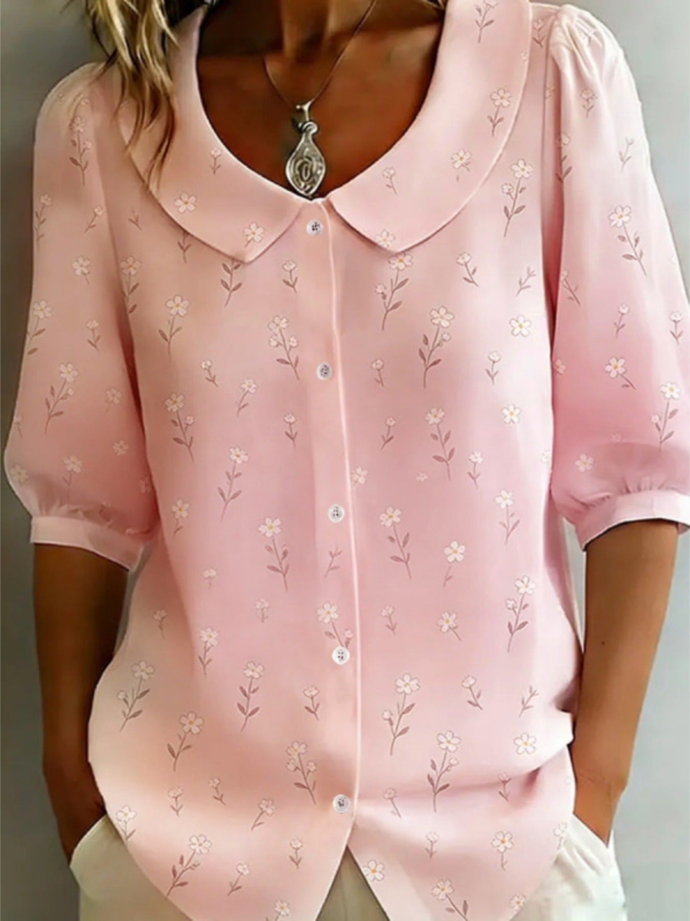 Pink blouse with floral pattern worn by a person against a neutral background