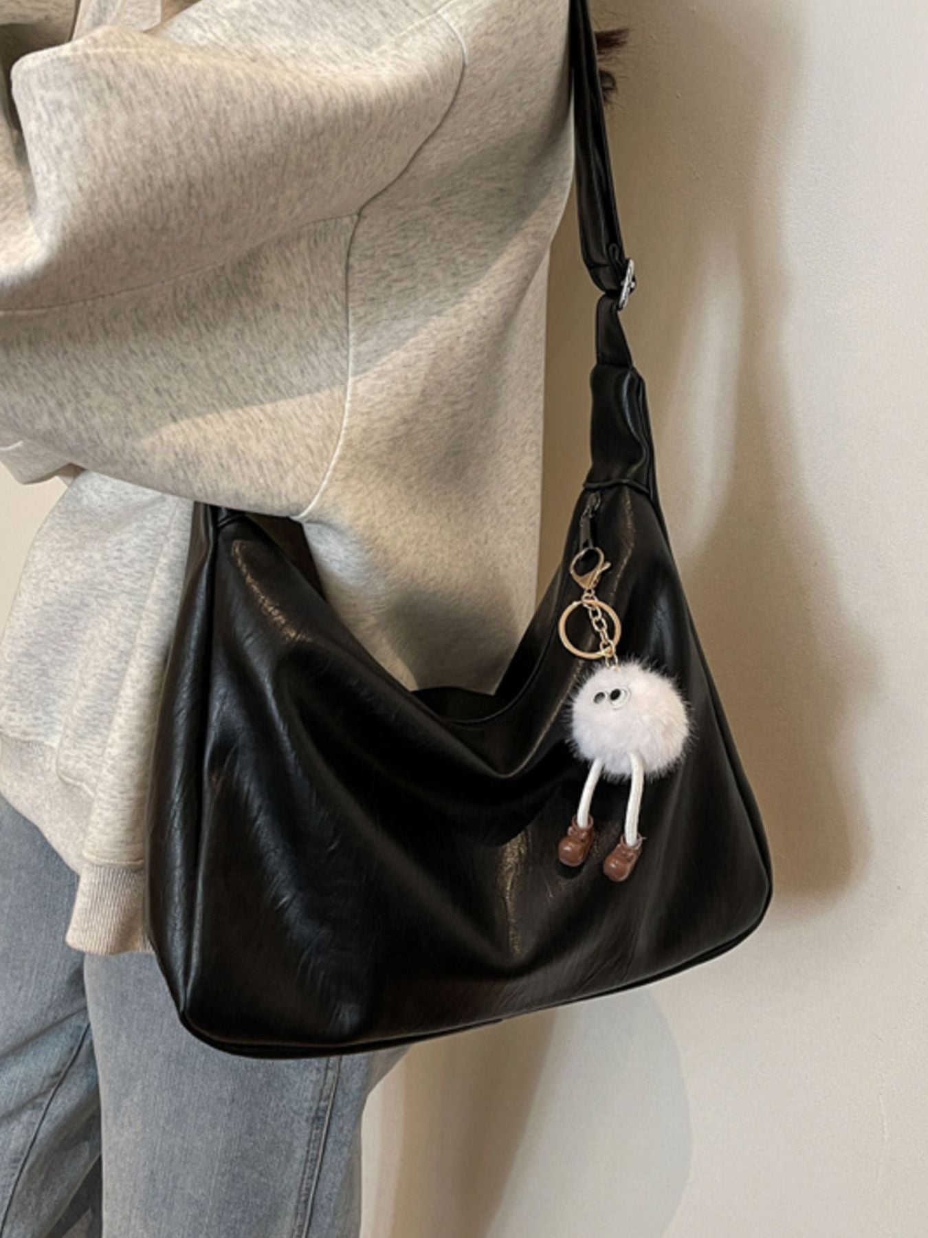 Black handbag with a fluffy keychain held by a person wearing a light gray sweater.