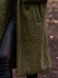 Green textured coat with leather sleeves against a blurred natural background