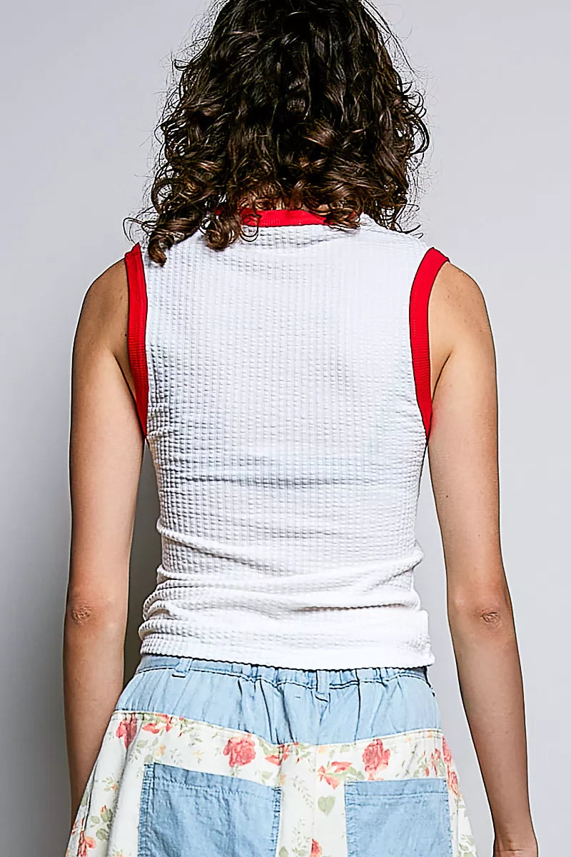 Person wearing a white sleeveless top with red straps and floral skirt on a plain background