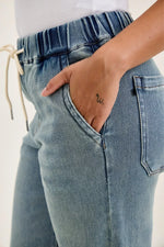 Close-up of blue jeans with a hand in the pocket on a plain background