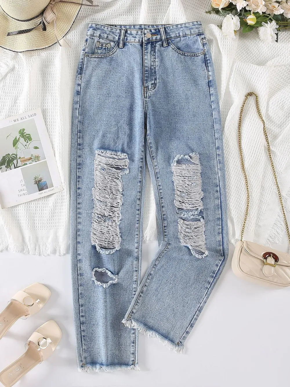 Ripped blue jeans on a white surface with accessories around