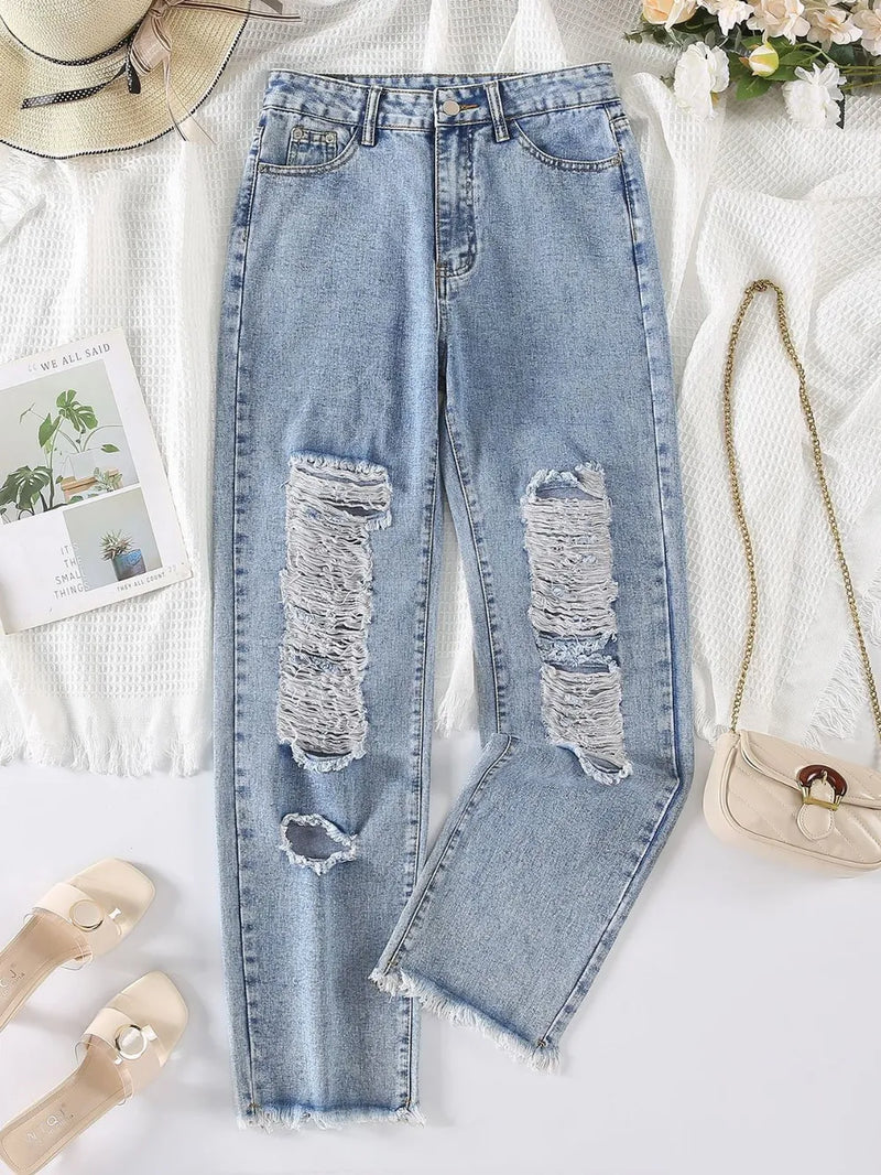 Ripped blue jeans on a white surface with accessories around
