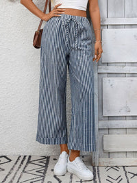 Person wearing blue and white striped pants with a white top against a light gray wall.