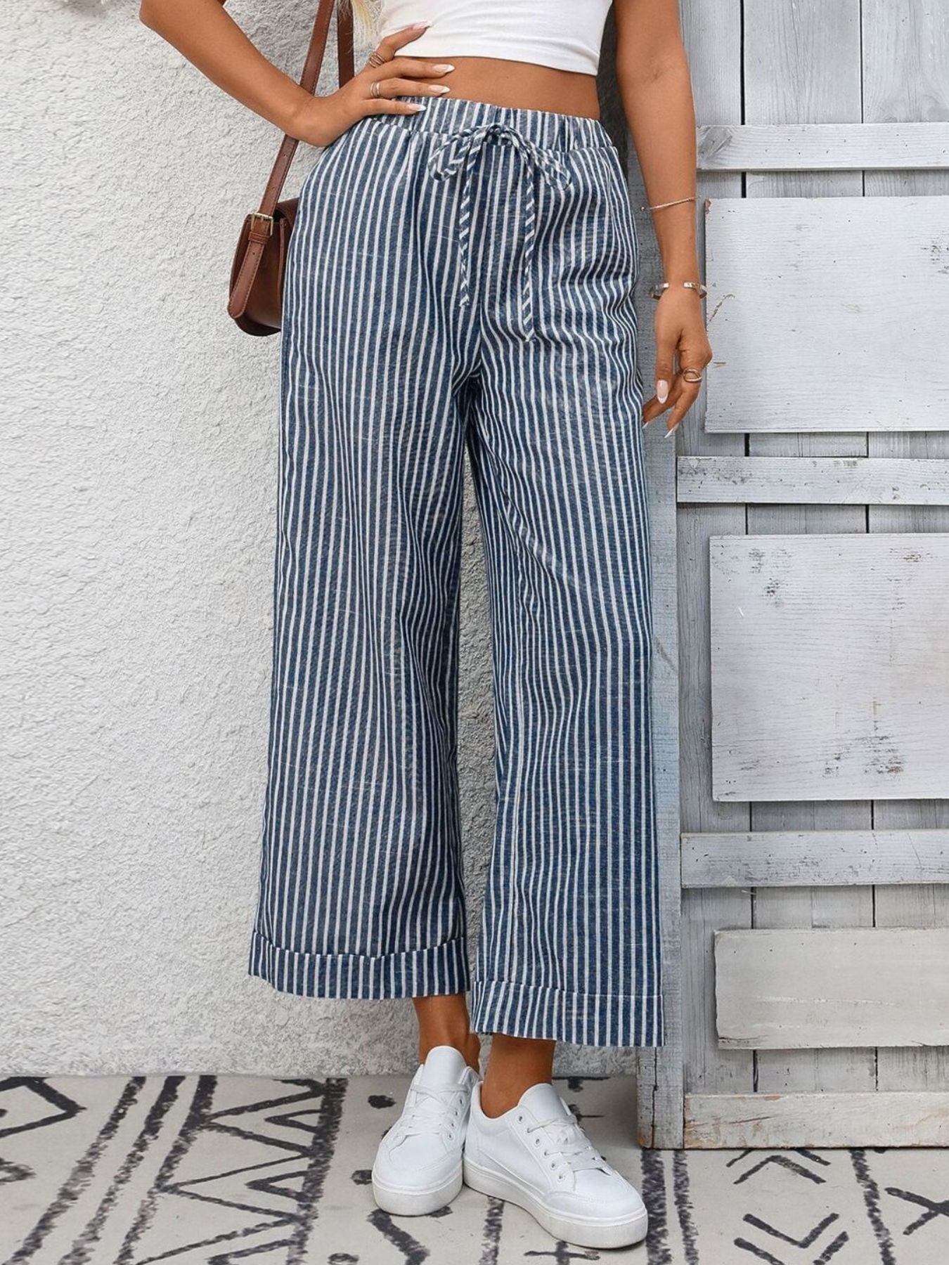 Person wearing blue and white striped pants with a white top against a light gray wall.