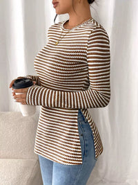 Person wearing a brown and beige striped sweater holding a coffee cup against a white curtain background