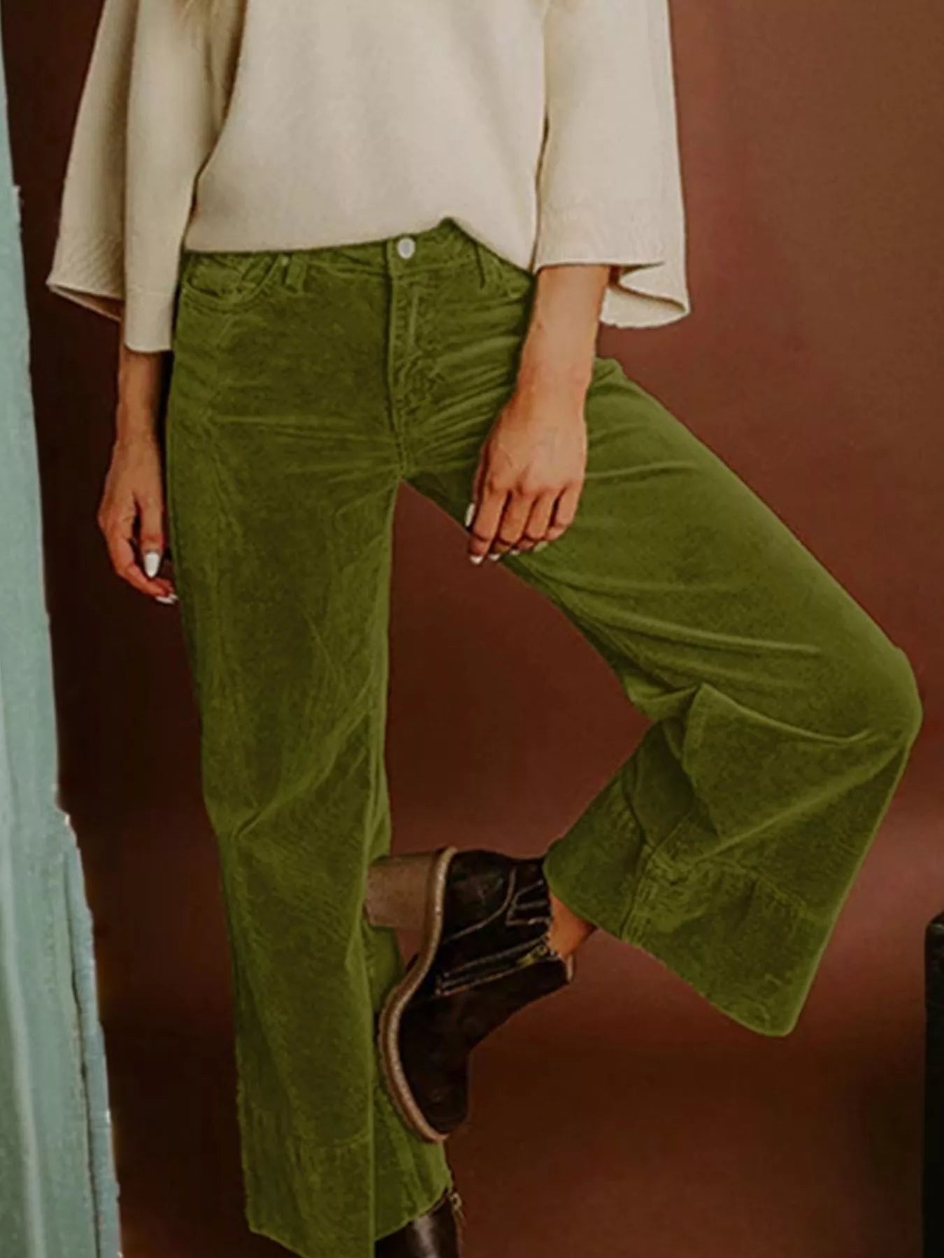 Person wearing green corduroy pants and a beige top against a brown background