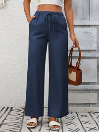 Person wearing navy wide-leg pants with a white top and brown handbag against a wooden panel background.