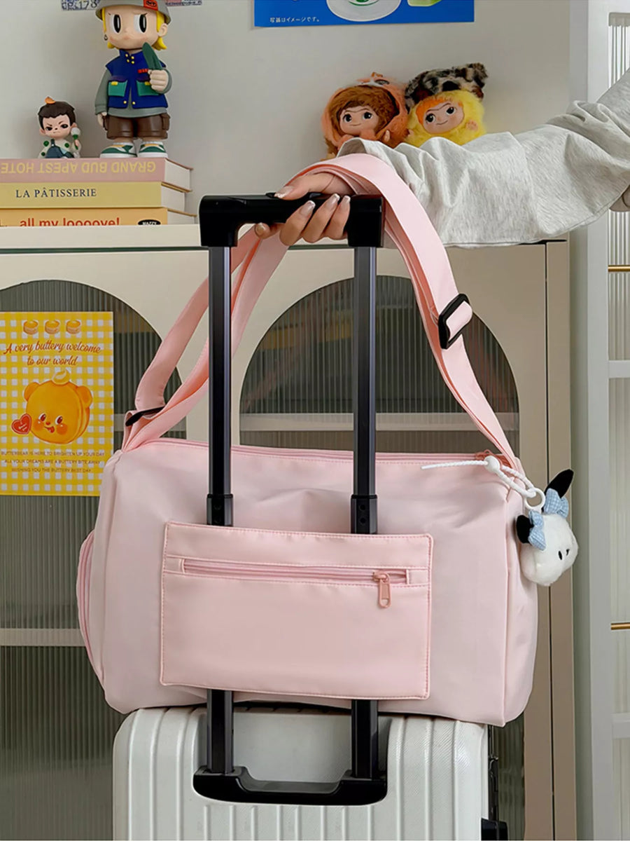 Pink duffel bag with a handle being held above a suitcase, with a shelf of books and figurines in the background.