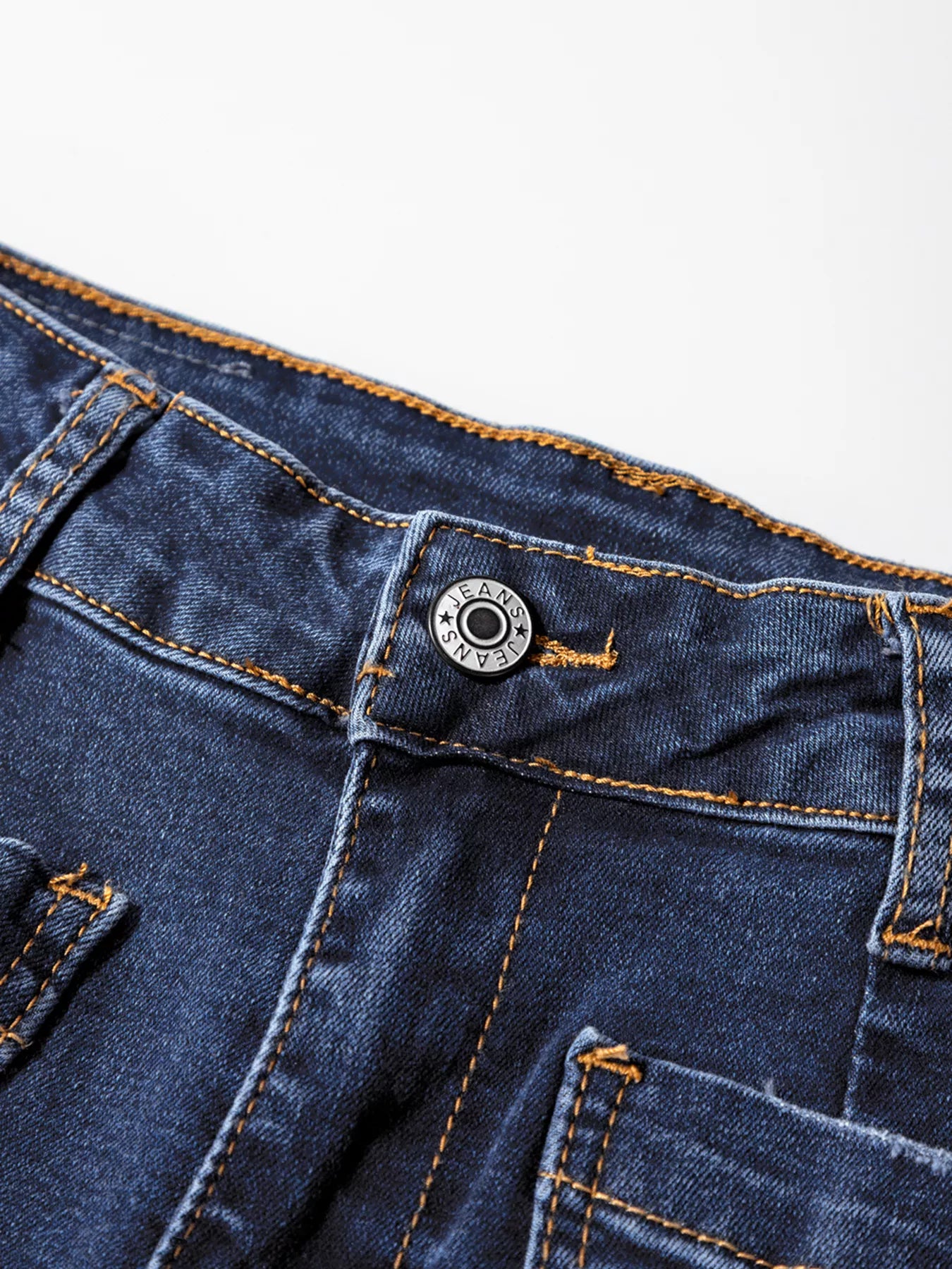 Close-up of blue denim jeans with a button and stitching detail on a white background