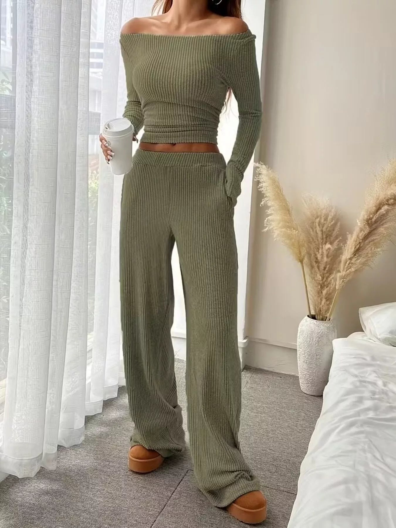 Person wearing a green ribbed knit outfit in a room with white curtains and a vase.