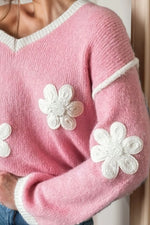 Pink sweater with white flower patterns on a neutral background