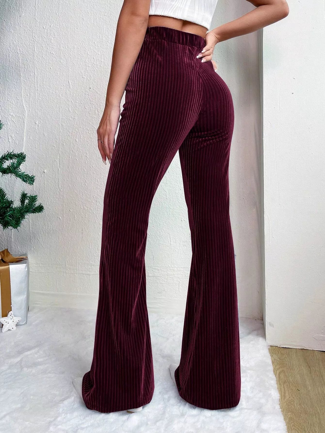 Person wearing burgundy ribbed flared pants with a white background