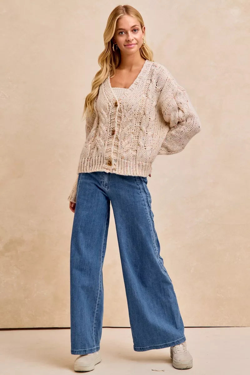 Woman wearing a beige cardigan and blue jeans against a beige background
