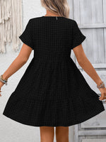 Black checkered dress worn by a person against a light gray wall.