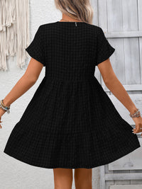 Black checkered dress worn by a person against a light gray wall.